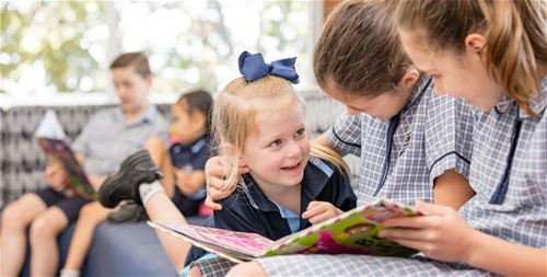 Students in school uniform reading a book together in a shared learning space.