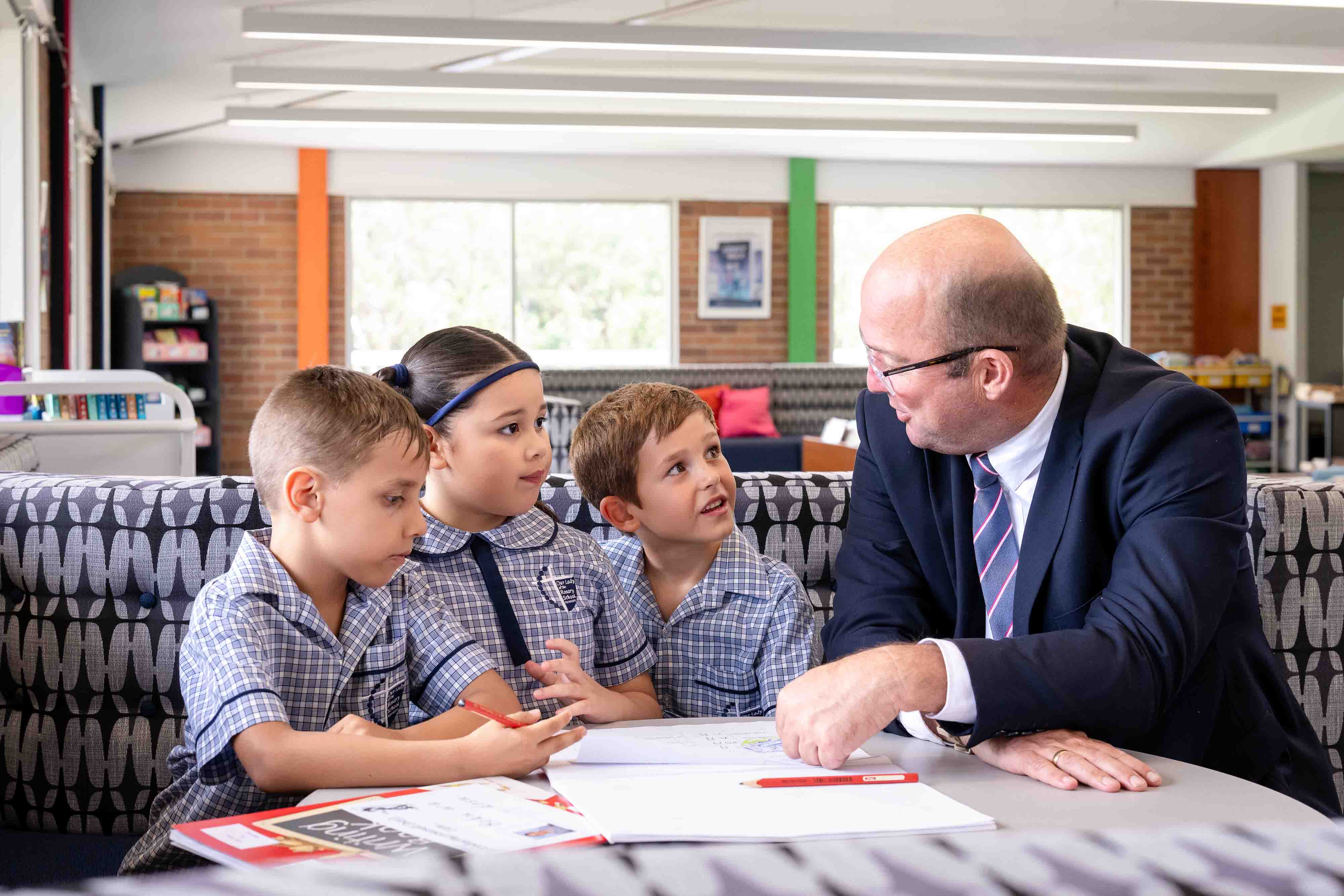 Adult seated at a table talking with three students in school uniform during a learning activity.