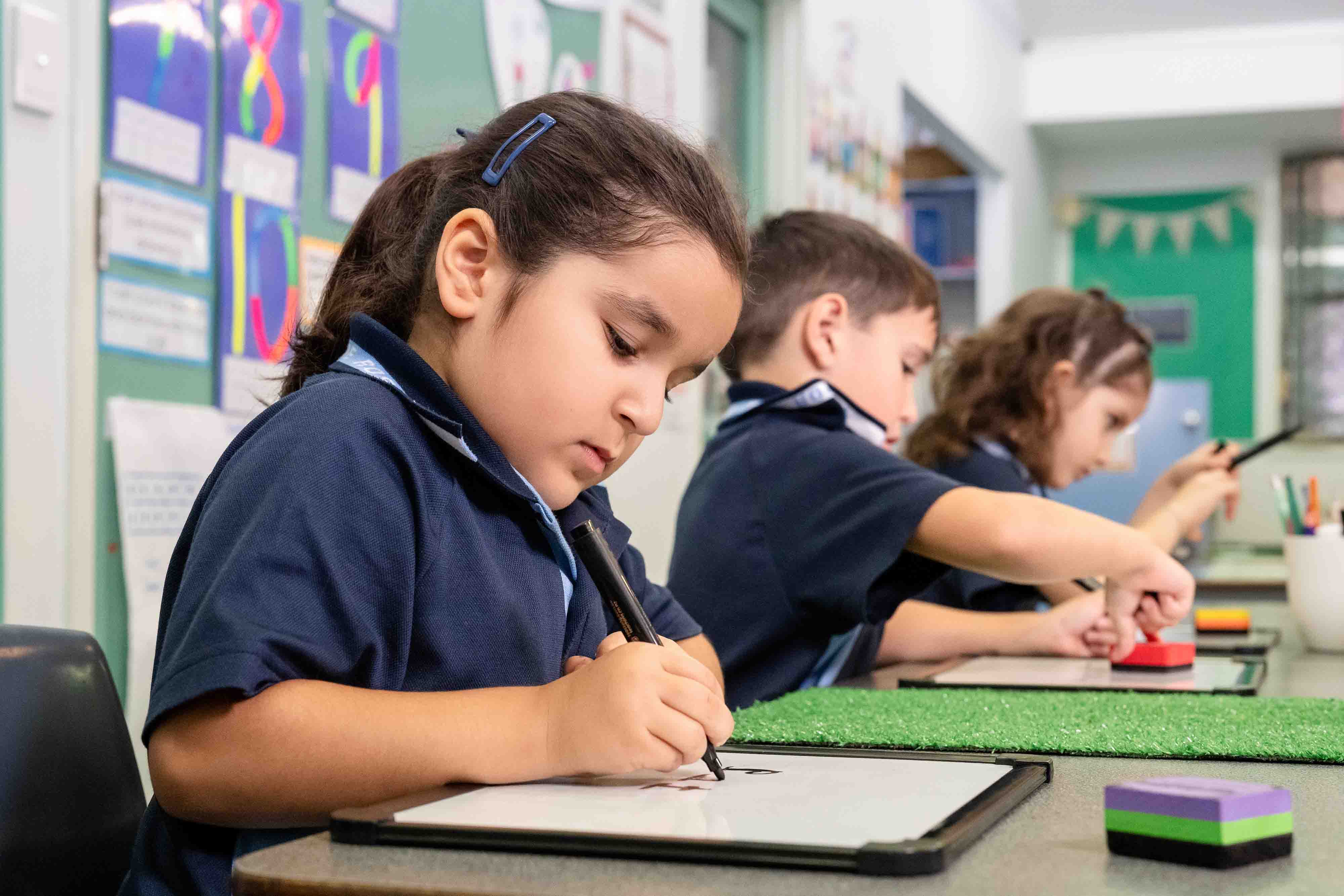 Students in school uniform writing on whiteboards during a classroom activity.