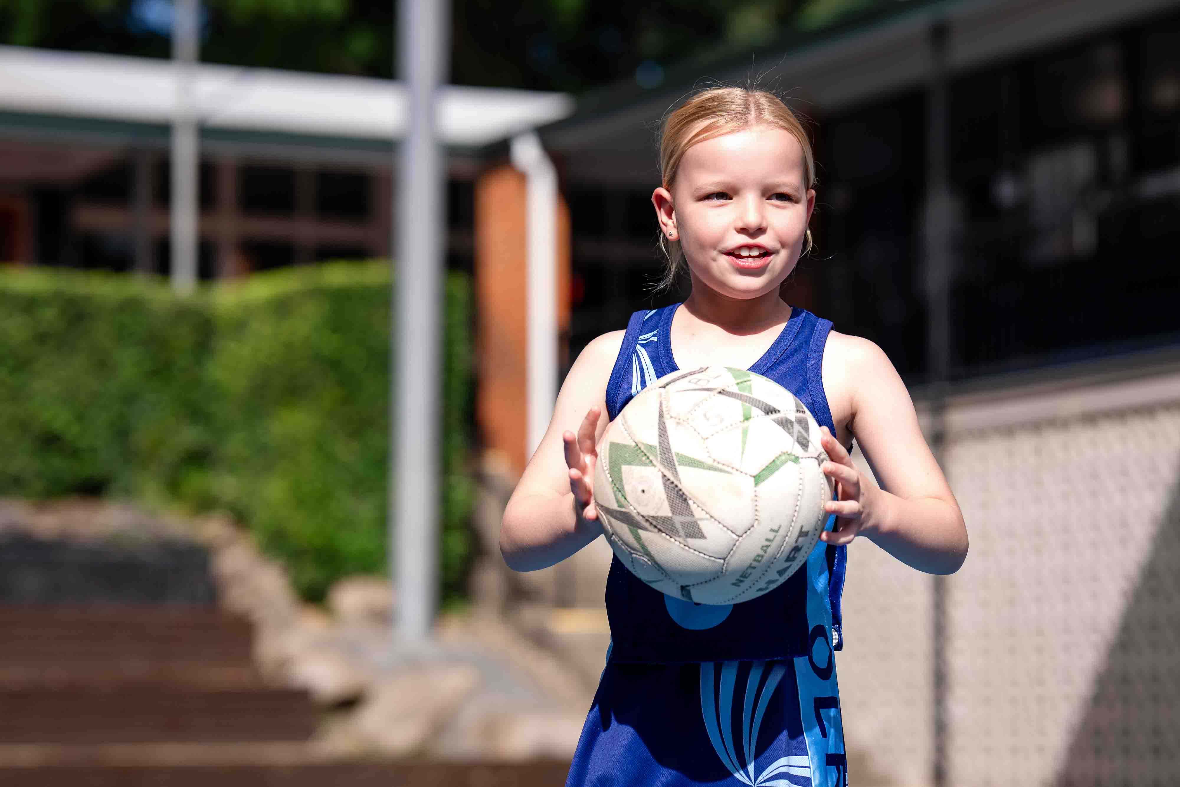 Student holding a netball outdoors on school grounds.