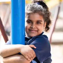 Student in school uniform holding onto a blue playground pole outdoors.