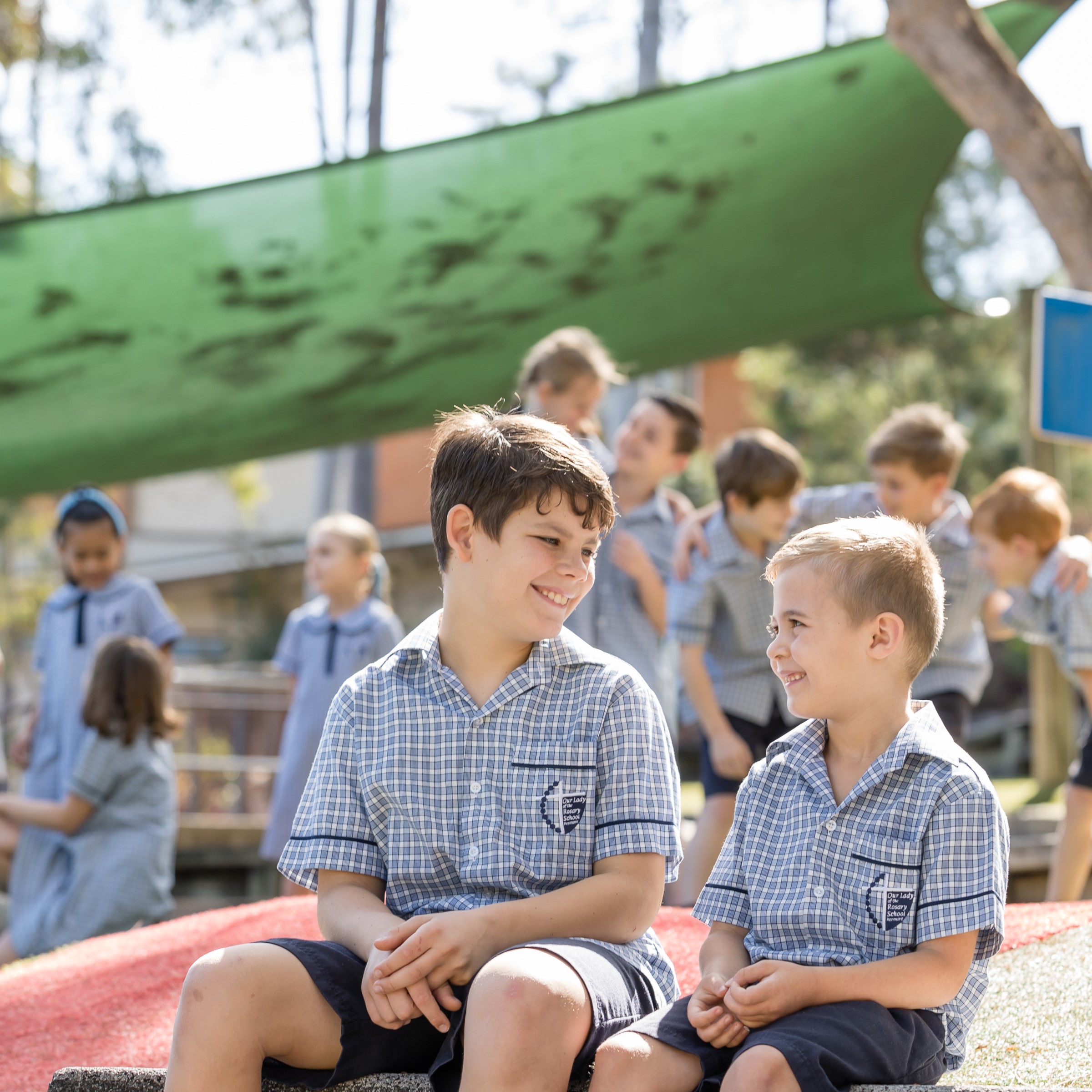 Students in school uniform sitting and playing in an outdoor school playground.