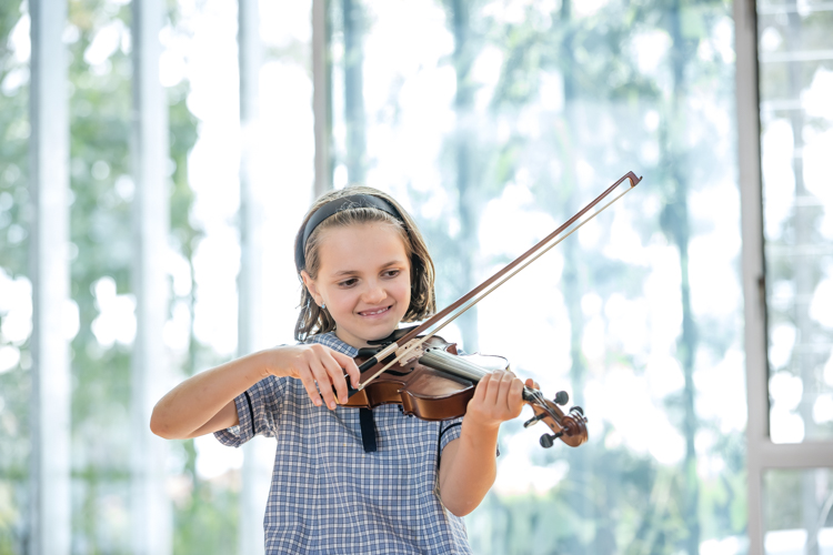 Student in school uniform playing a violin indoors.