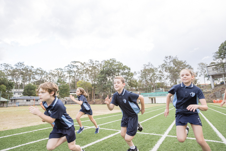 Students in school sports uniforms running on an outdoor athletics track.